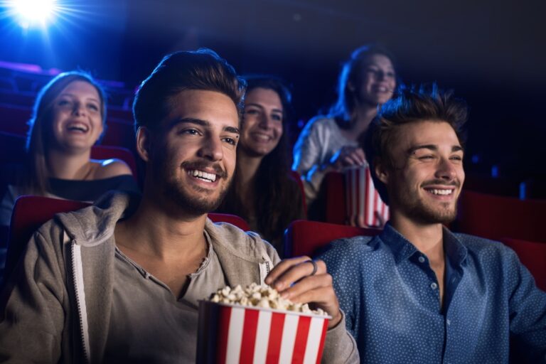 Friends laughing together in a cinema with a bucket of popcorn