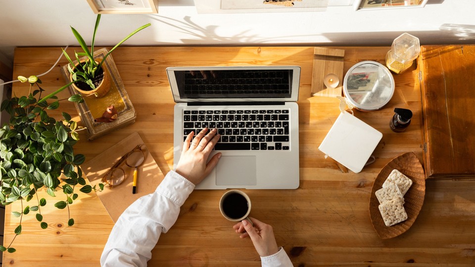 Overhead view of a person working on a laptop at a wooden desk with coffee and plants