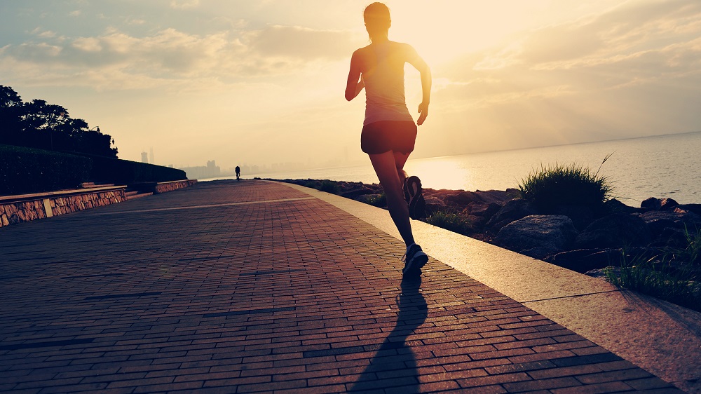 A woman jogging along a seaside promenade at sunrise