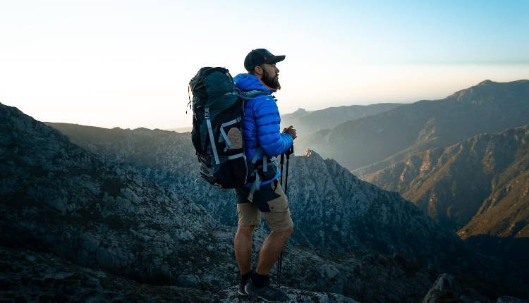 A backpacker with a large rucksack looking out over a mountain valley at dawn